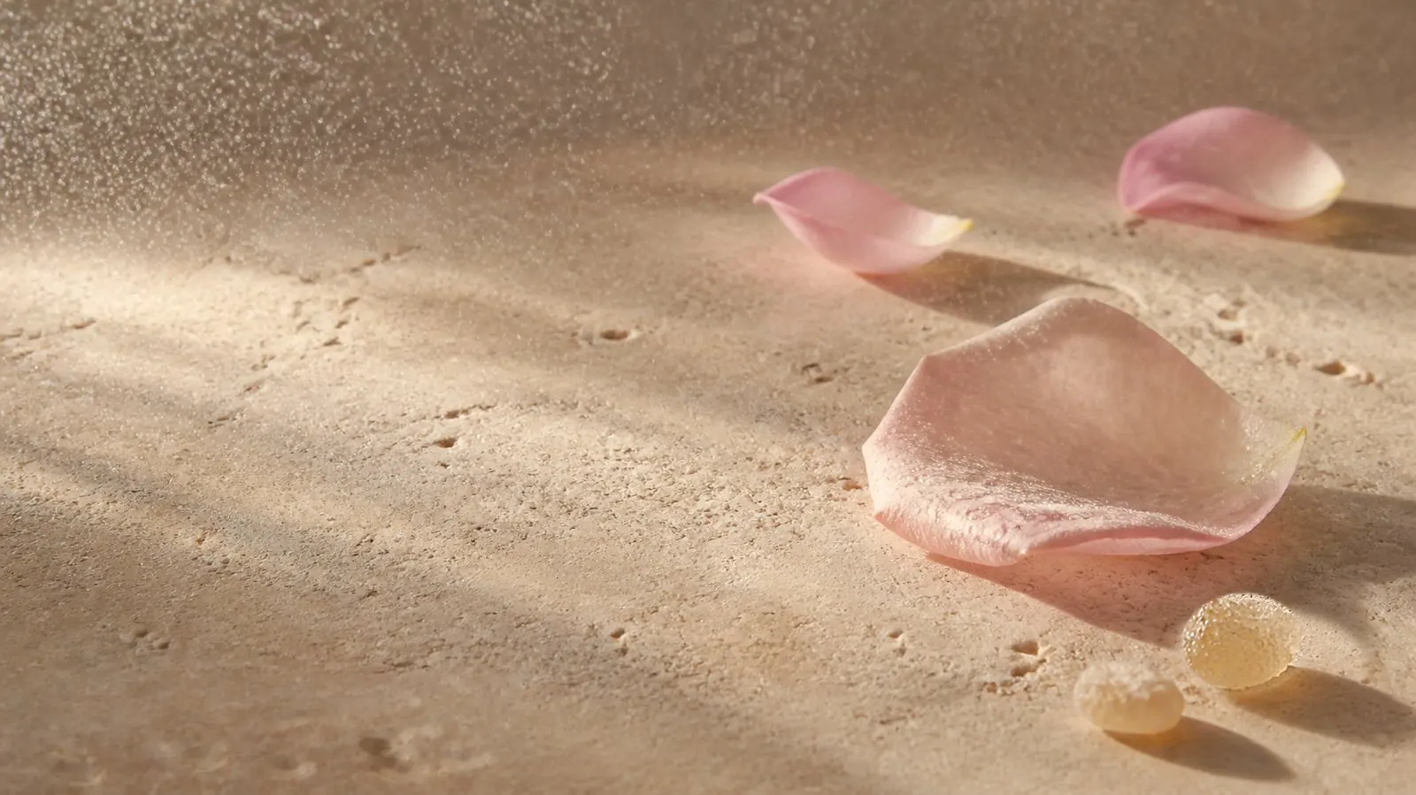 Bruma de agua de rosas suspendida en la luz sobre travertino, con pétalos de rosa y lágrimas de resina de olíbano